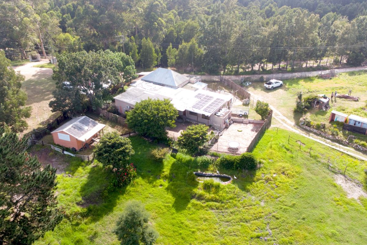 Aerial view of a farm property featuring a main residence with solar panels, an outbuilding, fenced grounds, and a small pond.