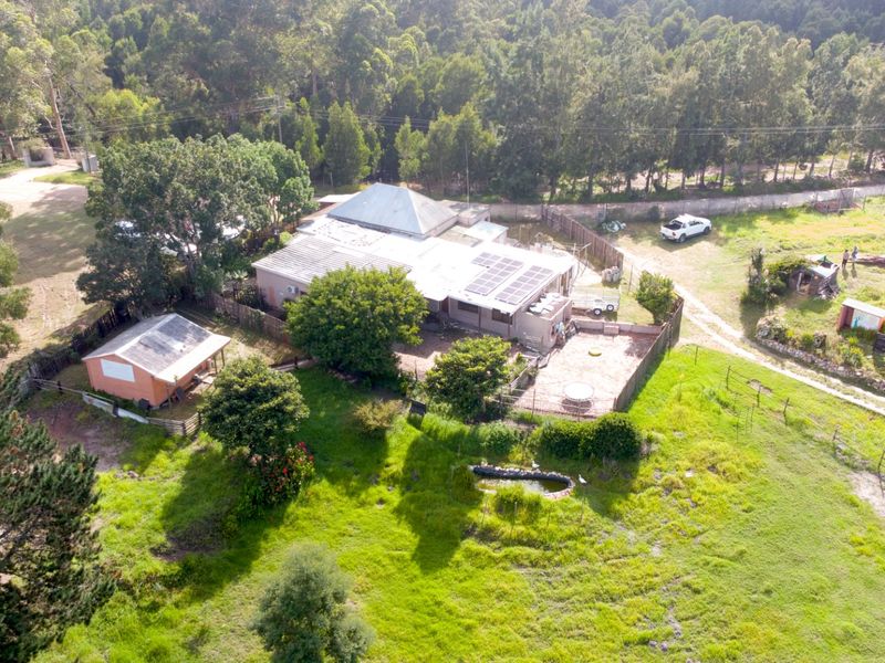 Aerial view of a farm property featuring a main residence with solar panels, an outbuilding, fenced grounds, and a small pond.