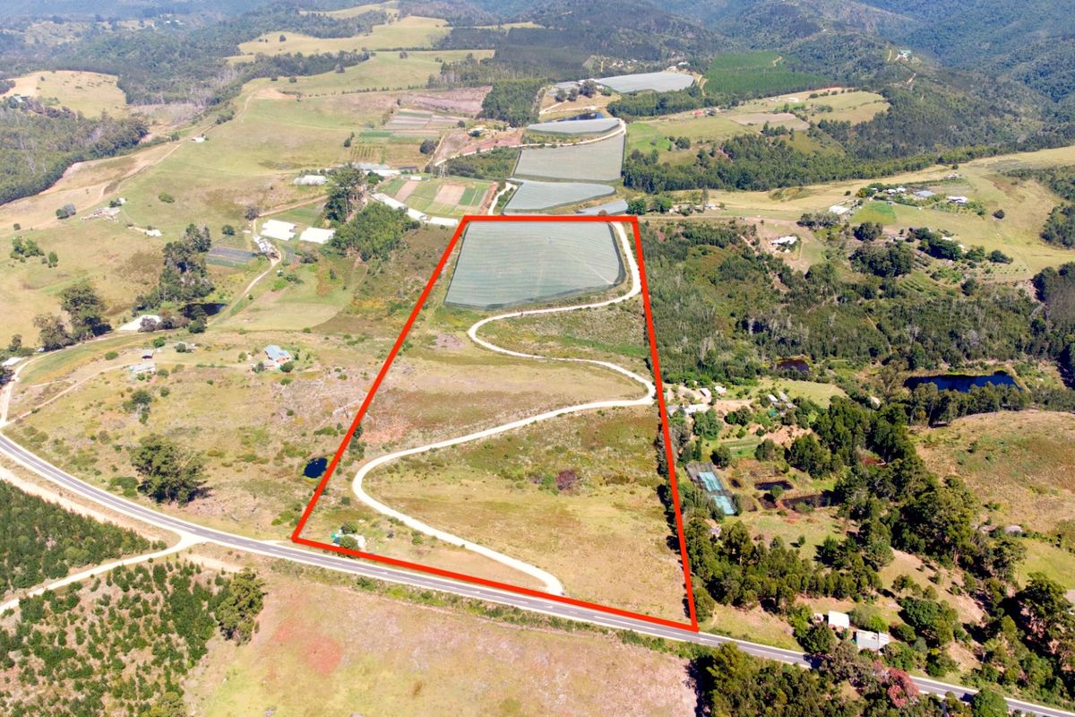 Aerial view of a large farm property featuring a winding driveway, agricultural netting, and expansive open land with surrounding rural landscape.