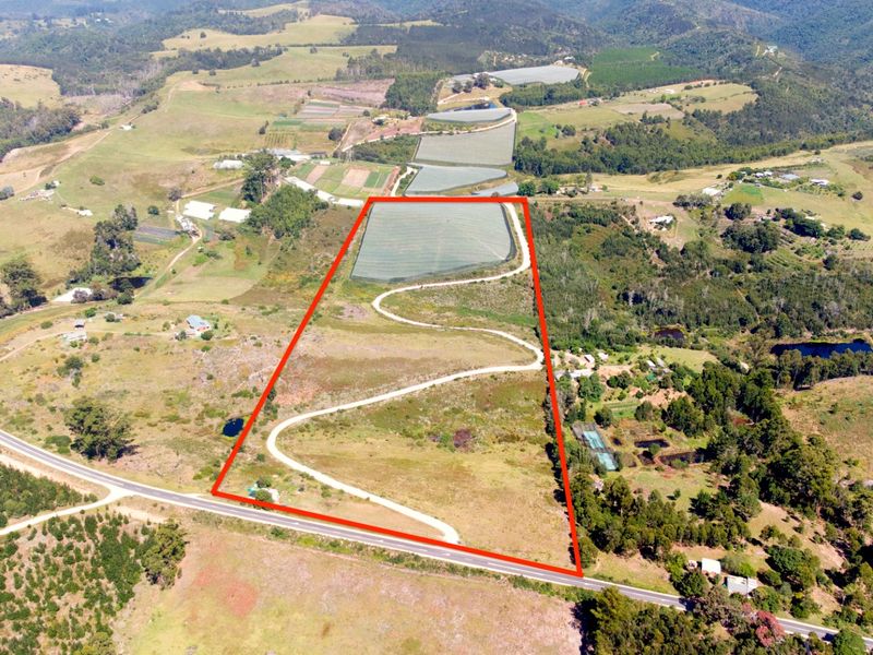 Aerial view of a large farm property featuring a winding driveway, agricultural netting, and expansive open land with surrounding rural landscape.