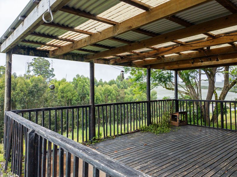 A spacious covered timber deck featuring a balustrade and corrugated roof, offering expansive views of the surrounding rural landscape.