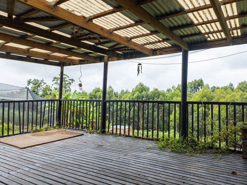 A spacious covered timber deck featuring a balustrade and corrugated roof, offering an elevated view of the surrounding farm landscape.