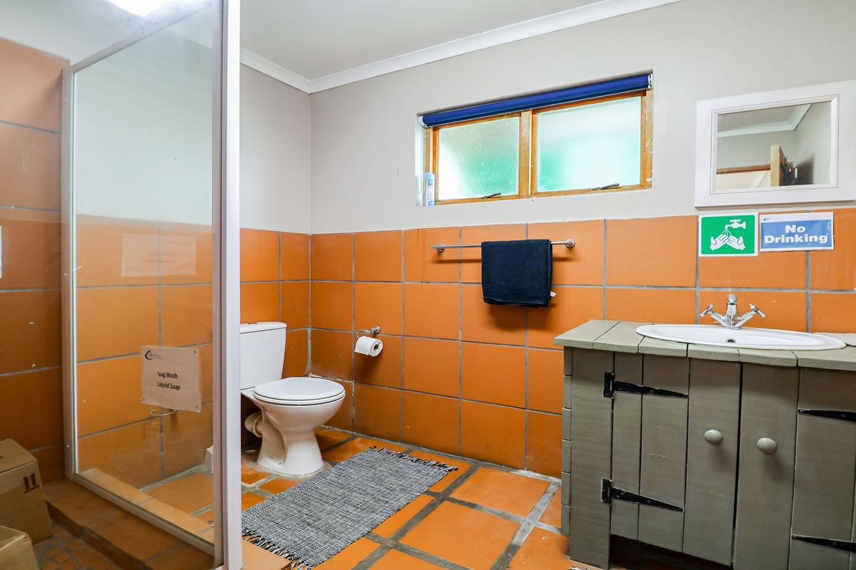 A functional bathroom featuring a shower enclosure, toilet, and a rustic vanity cabinet with a basin, finished with orange wall and floor tiles.