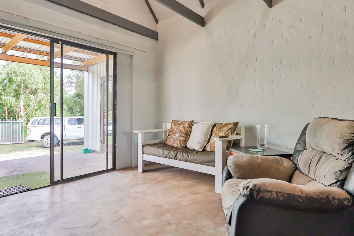 A rustic living area featuring exposed timber ceiling beams, painted brick walls, and concrete flooring, with direct access to an outdoor patio area.