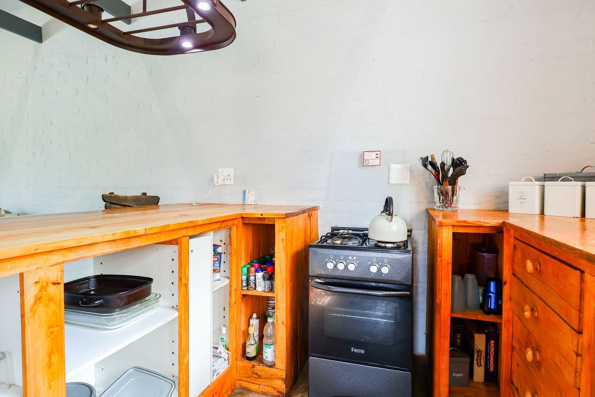 A rustic kitchen area featuring wooden cabinetry, a freestanding gas stove, and exposed ceiling beams against painted brick walls.