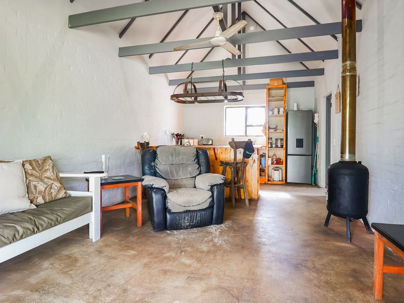 Open-plan living area featuring exposed timber beams, a freestanding wood-burning fireplace, and a functional kitchen space with concrete flooring throughout.