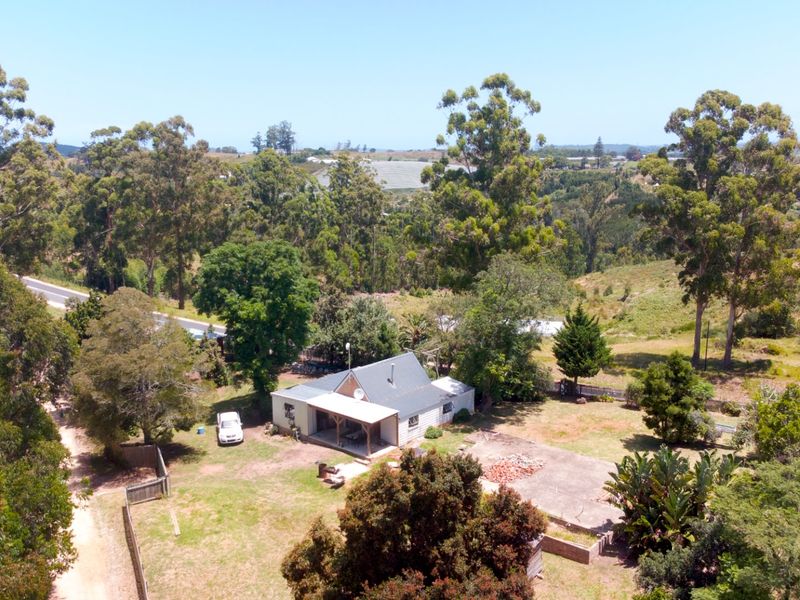 Aerial view of a rural farm property featuring a dwelling with a covered patio, concrete slab area, and surrounding natural landscape.