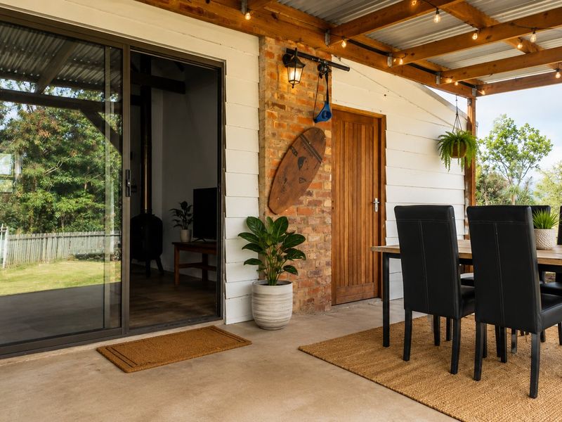 A covered outdoor patio featuring exposed timber rafters, a brick chimney feature, and sliding glass doors leading into the main living area.