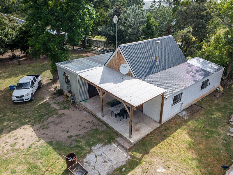 Aerial view of a farm-style dwelling featuring a corrugated metal roof, a covered patio area, and surrounding garden space.