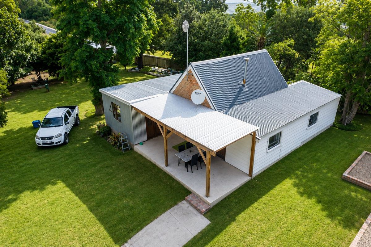 Aerial view of a farm-style dwelling featuring a corrugated metal roof, a covered patio area, and surrounding green lawn.