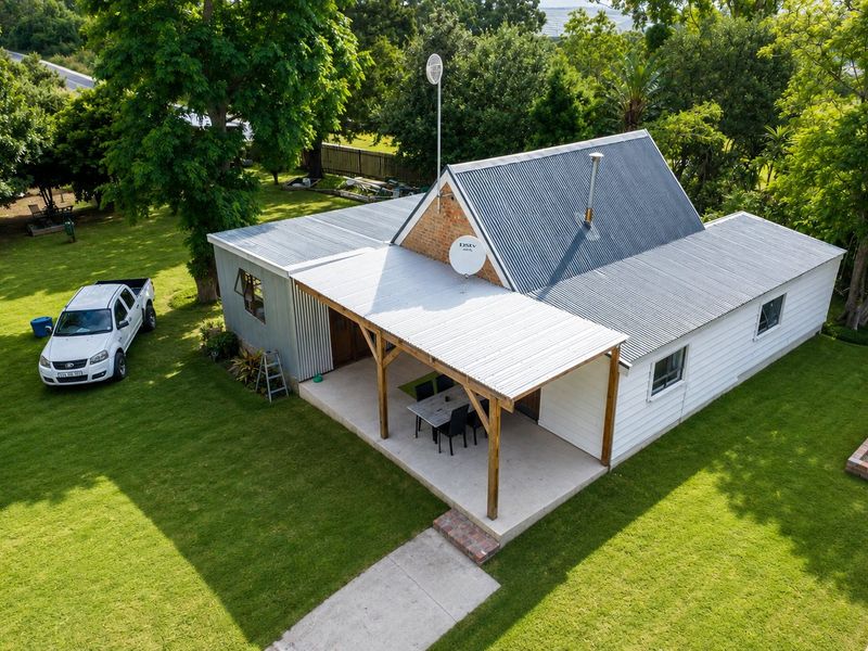 Aerial view of a farm-style dwelling featuring a corrugated metal roof, a covered patio area, and surrounding green lawn.