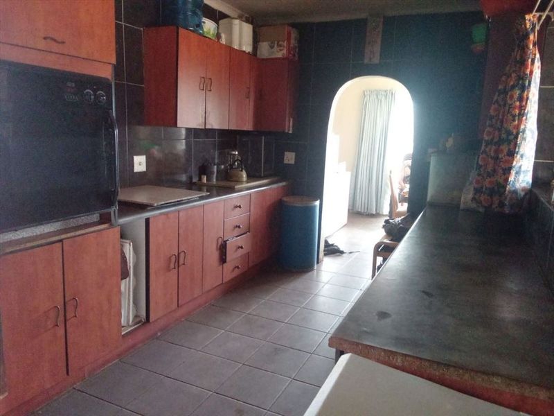 A dated kitchen featuring dark tiled walls, wooden cabinetry, and a built-in oven, leading through an archway to an adjacent living space.