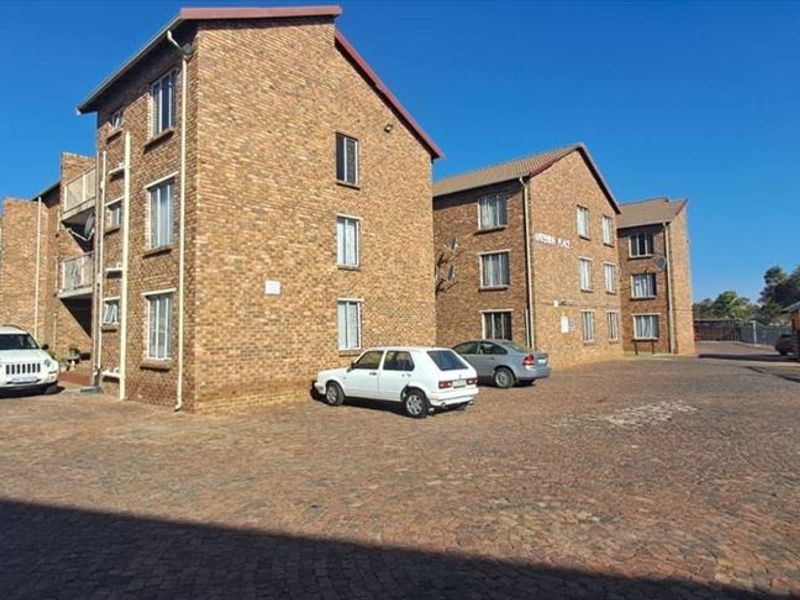 Exterior view of a multi-story face-brick apartment complex featuring a paved driveway and secure gated entrance.