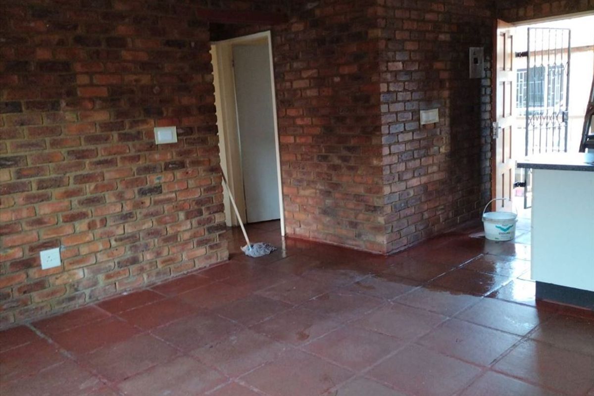 Open plan living area featuring exposed brick walls and terracotta floor tiles, with direct access to an exterior entrance.