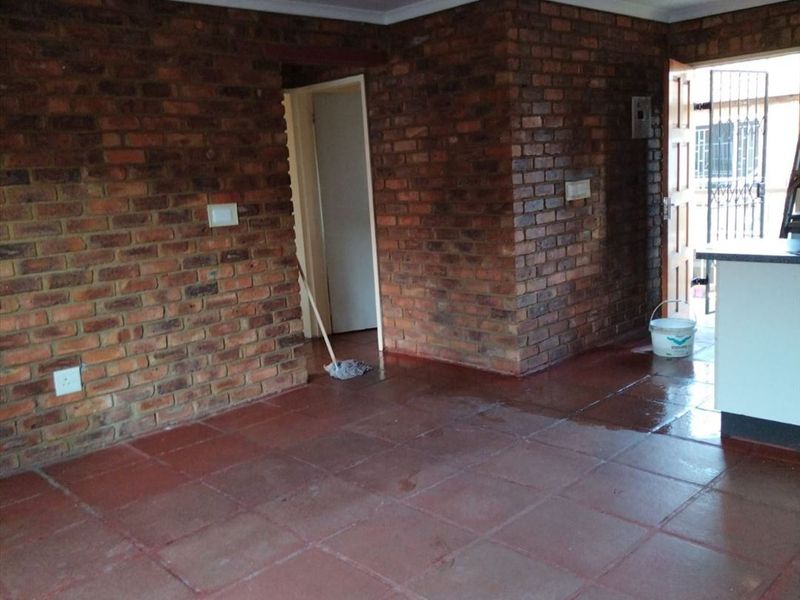 Open plan living area featuring exposed brick walls and terracotta floor tiles, with direct access to an exterior entrance.