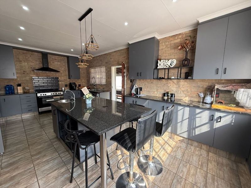 Modern kitchen featuring dark grey cabinetry, granite countertops, a central island, and exposed brick walls, creating a stylish and functional culinary space.