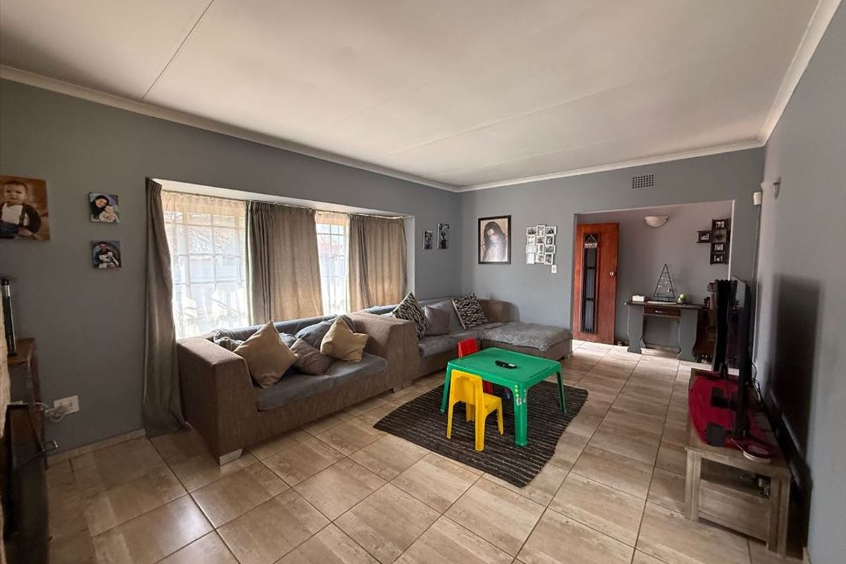 Spacious living room featuring large bay windows, neutral tiled flooring, and coved ceiling details, offering a comfortable and functional family living space.