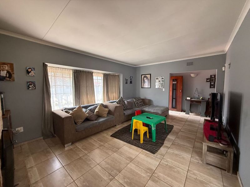 Spacious living room featuring large bay windows, neutral tiled flooring, and coved ceiling details, offering a comfortable and functional family living space.