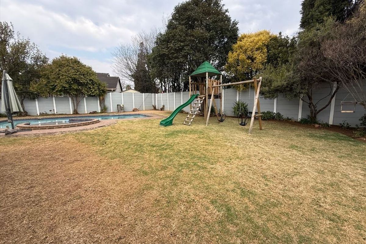 A spacious backyard featuring a swimming pool with brick coping, a lawn area, and perimeter precast concrete walling.
