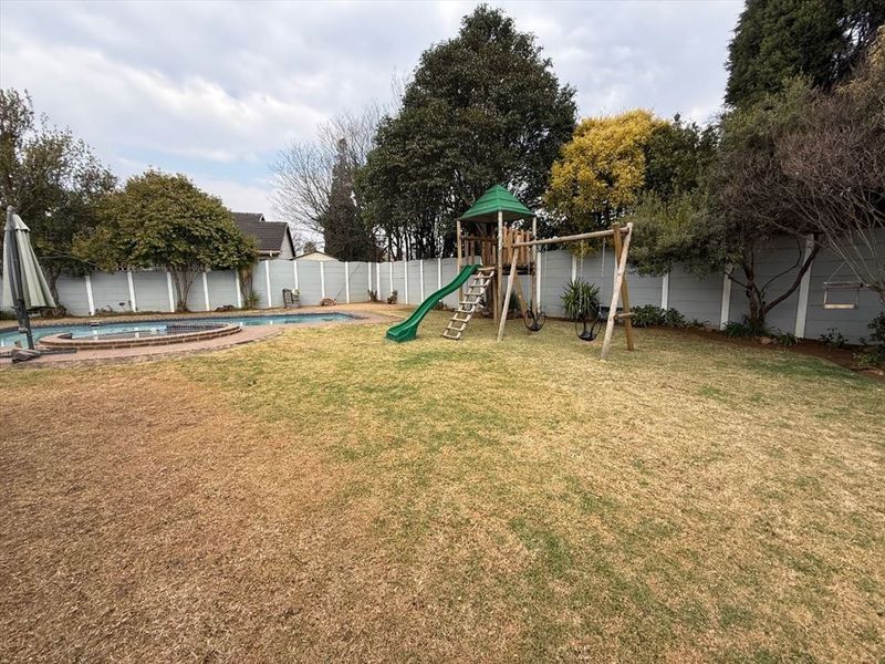 A spacious backyard featuring a swimming pool with brick coping, a lawn area, and perimeter precast concrete walling.