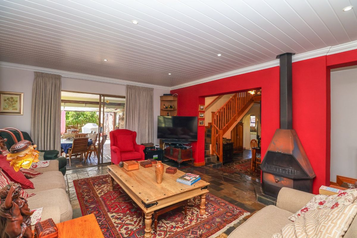 Spacious living room featuring a striking red accent wall, a modern freestanding fireplace, slate flooring, and direct access to an outdoor patio area.