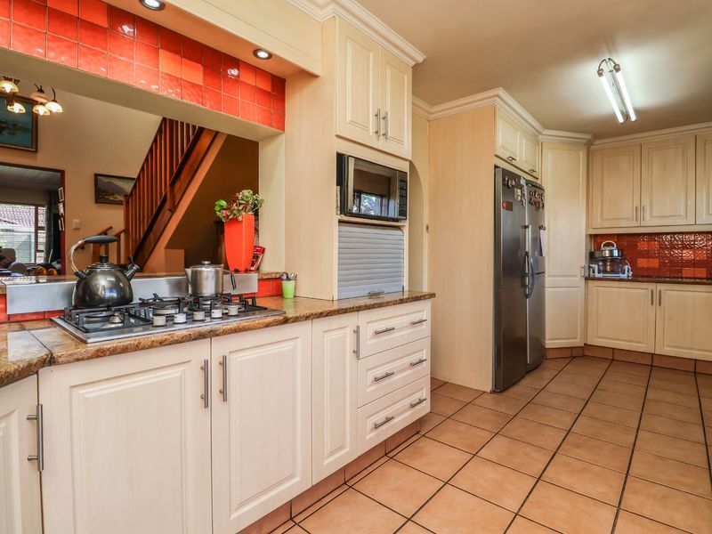 A functional kitchen featuring light-toned cabinetry, granite countertops, a gas hob, and a vibrant tiled backsplash, with an open-plan view toward the staircase.