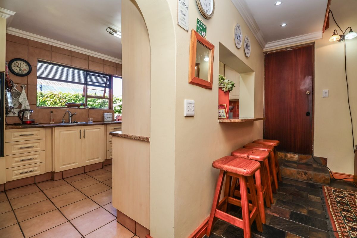A functional kitchen featuring built-in cabinetry, laminate countertops, and a breakfast bar opening into an adjacent living area with tiled flooring throughout.
