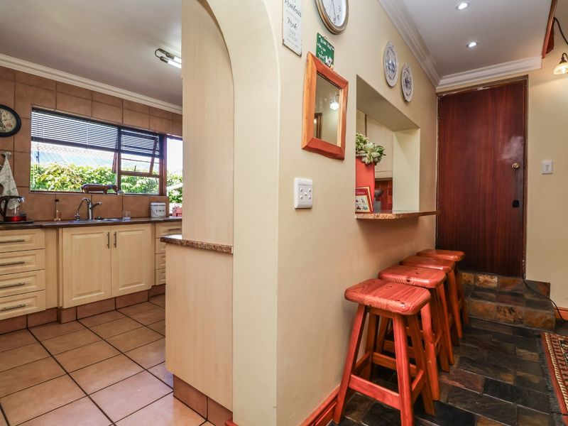 A functional kitchen featuring built-in cabinetry, laminate countertops, and a breakfast bar opening into an adjacent living area with tiled flooring throughout.
