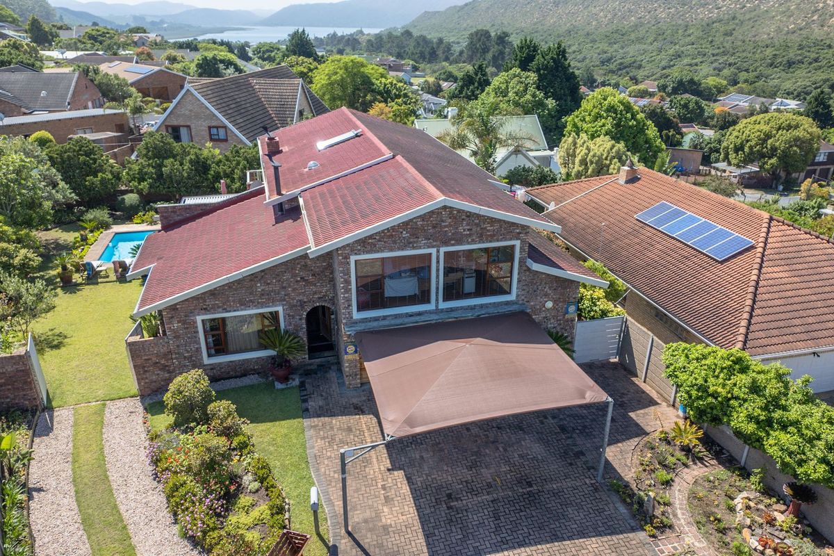 Aerial view of a brick-faced house featuring a tiled roof, paved driveway with a shade sail carport, and a private swimming pool in the garden.