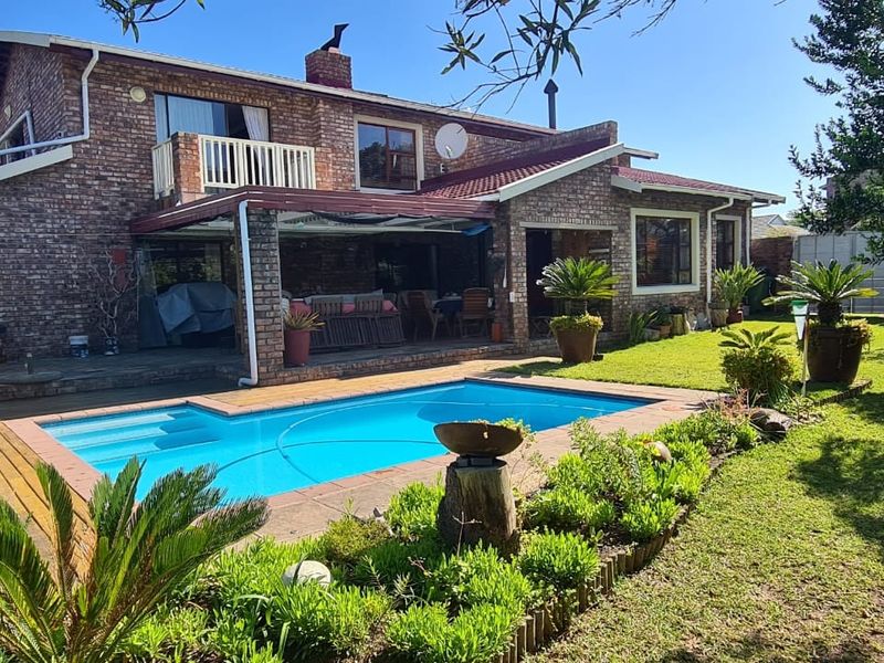Rear view of a double-story brick house featuring a swimming pool, covered patio, and a well-maintained garden.