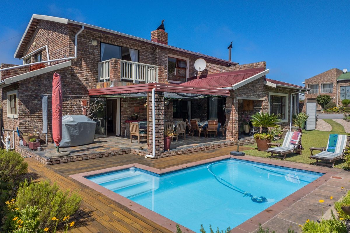 Rear view of a brick house featuring a swimming pool, timber decking, and a covered patio area.