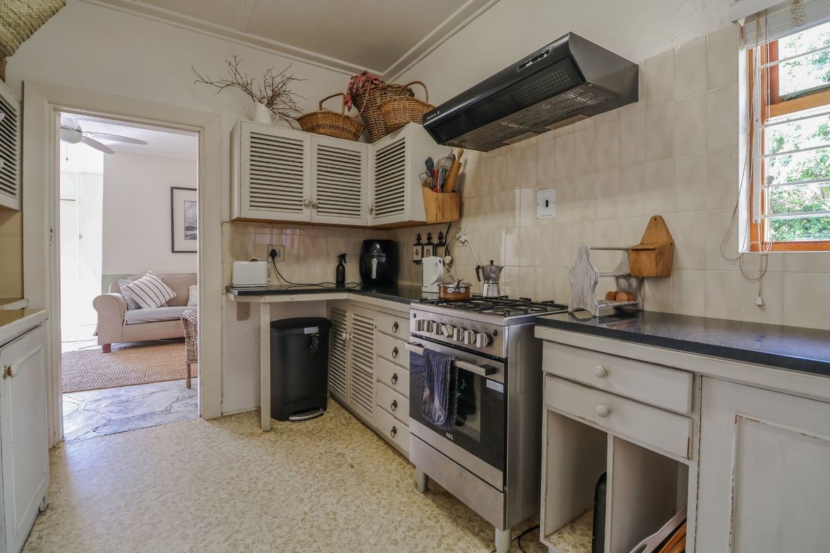 A functional kitchen featuring a gas stove, extractor fan, tiled backsplash, and louvered cabinetry, with a view into the adjacent living area.