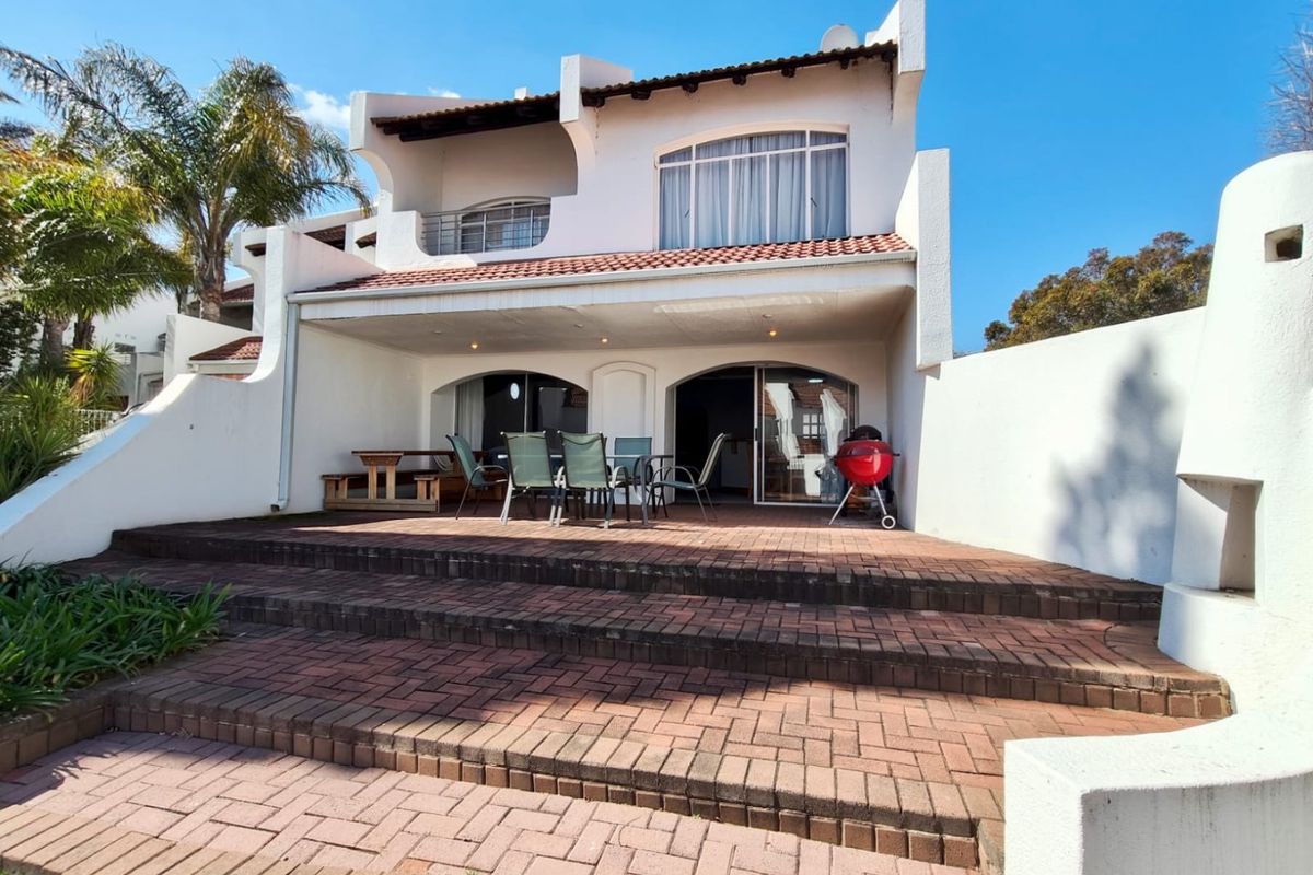 Rear view of the townhouse featuring a paved patio area, covered terrace, and upper-level balcony with traditional terracotta roof tiles.