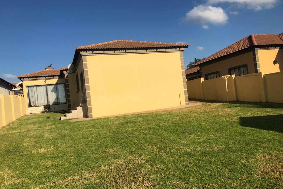 Rear view of the house featuring a private lawn, perimeter wall, and tiled roof structure with a sliding door entrance.