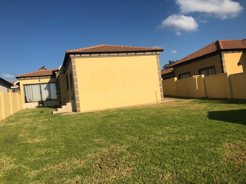 Rear view of the house featuring a private lawn, perimeter wall, and tiled roof structure with a sliding door entrance.