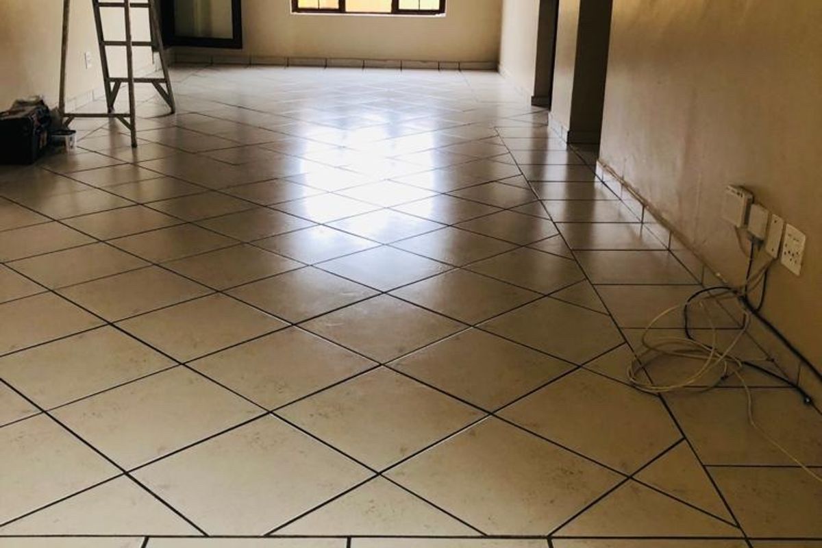 An empty, open-plan living area featuring tiled flooring, neutral walls, and aluminium window and door frames, ready for renovation or staging.