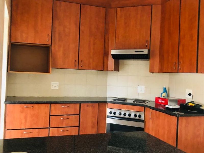 A functional kitchen featuring wooden cabinetry, granite countertops, and built-in cooking appliances including an oven and hob.