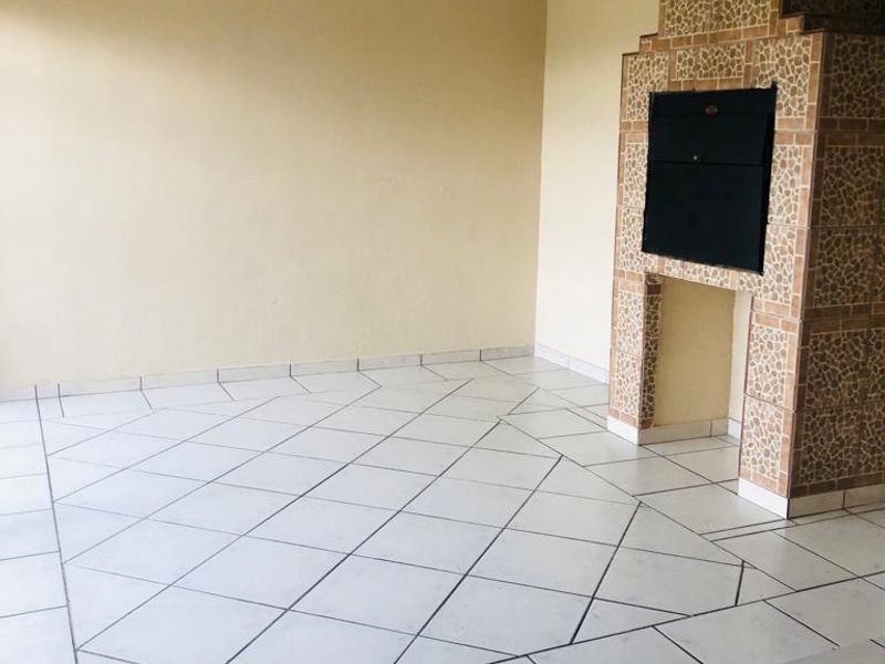 An empty covered patio area featuring tiled flooring and a built-in brick braai, offering a versatile space for outdoor entertainment.