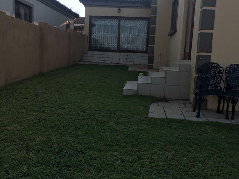 Rear view of the property featuring a small lawn, tiled patio area, and secure access points with boundary walling.
