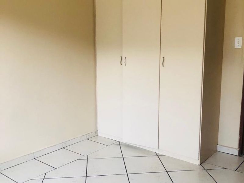 A clean, empty bedroom featuring neutral wall paint, ceramic floor tiles, and a built-in wardrobe.