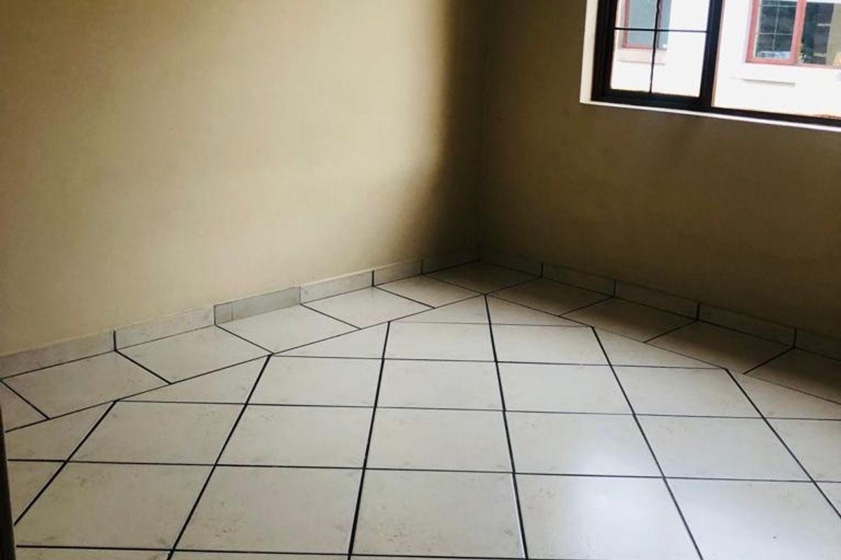 An empty bedroom featuring tiled flooring and a window with security bars, requiring minor cosmetic updates to improve its overall appeal.