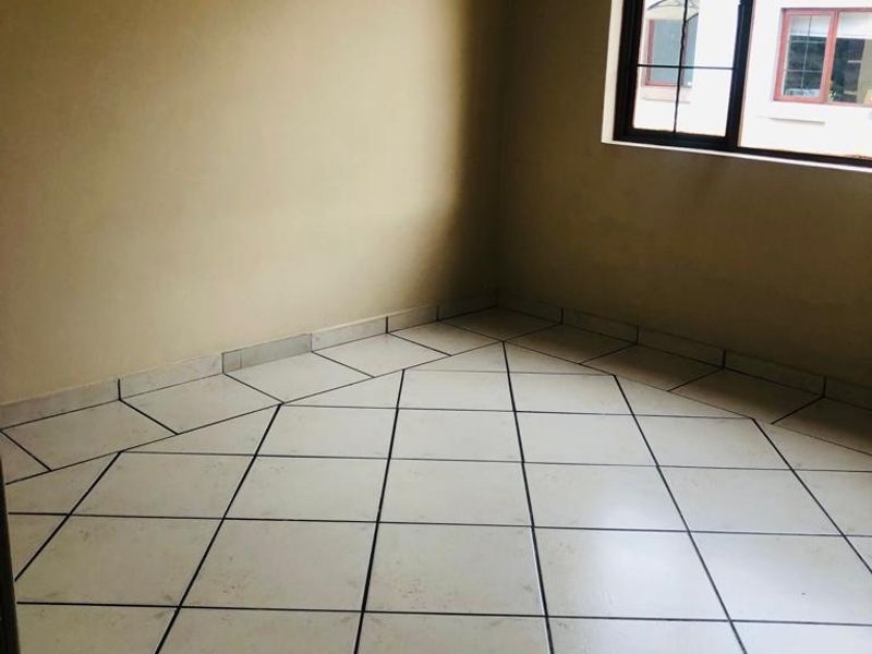 An empty bedroom featuring tiled flooring and a window with security bars, requiring minor cosmetic updates to improve its overall appeal.