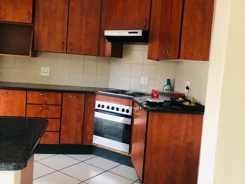 A functional kitchen featuring wooden cabinetry, granite countertops, a built-in oven with hob, and tiled flooring.