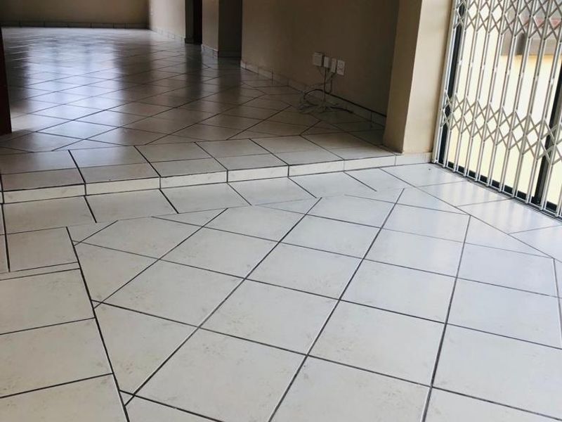 Spacious open-plan living area featuring ceramic tiled flooring, a raised floor section, and a secure sliding door leading to the exterior.