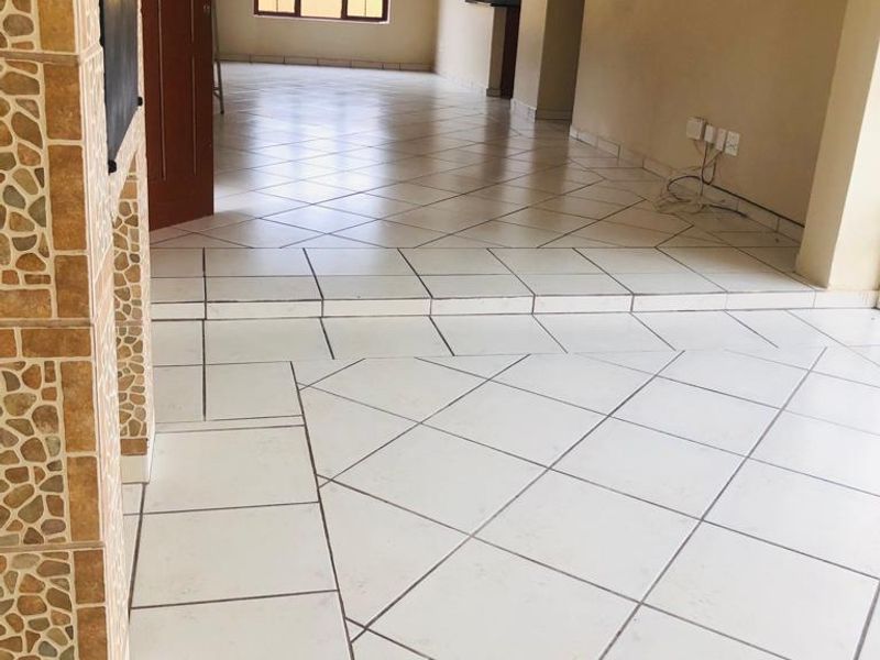 An open-plan living area featuring a sunken floor design, neutral tiled flooring, and a decorative tiled pillar.