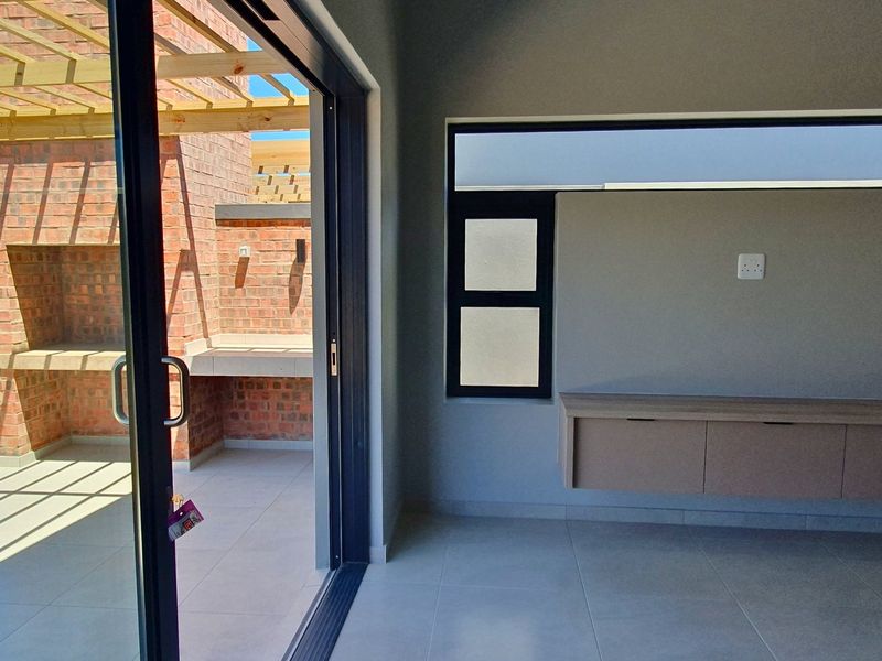 Modern open-plan living area featuring tiled floors, built-in cabinetry, and seamless access to a private patio with a brick built-in braai and pergola.
