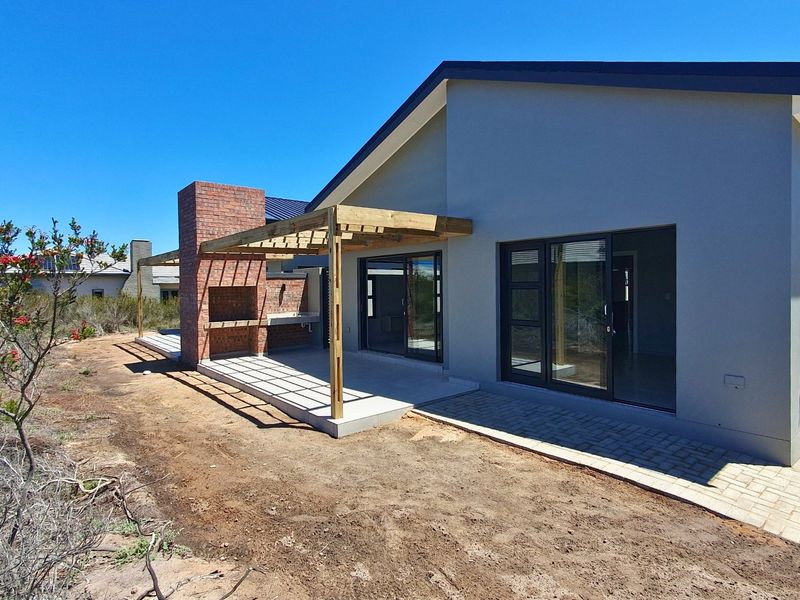 Rear exterior view of a townhouse featuring a covered patio with a built-in brick braai, timber pergola, and sliding glass door access.