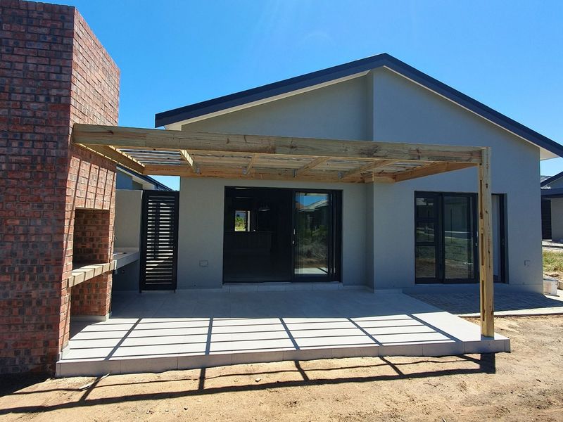 A modern covered patio featuring a built-in brick braai, timber pergola structure, and tiled flooring, providing a seamless transition to the interior living space.