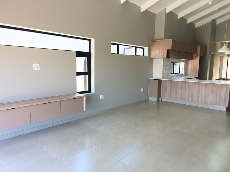 Spacious open-plan living and kitchen area featuring modern built-in cabinetry, tiled flooring, and high exposed beam ceilings in a contemporary townhouse setting.