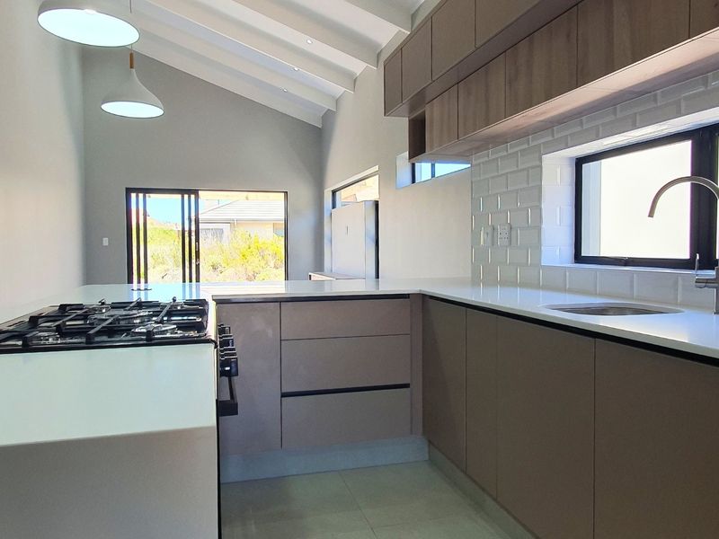 Modern kitchen featuring quartz countertops, gas hob, subway tile backsplash, and vaulted ceilings with exposed rafters, leading to an open-plan living area.